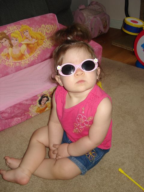 2000 Ford Crown Victoria - A baby girl sits on a carpeted floor, sporting pink sunglasses and a pink top with floral embroidery.