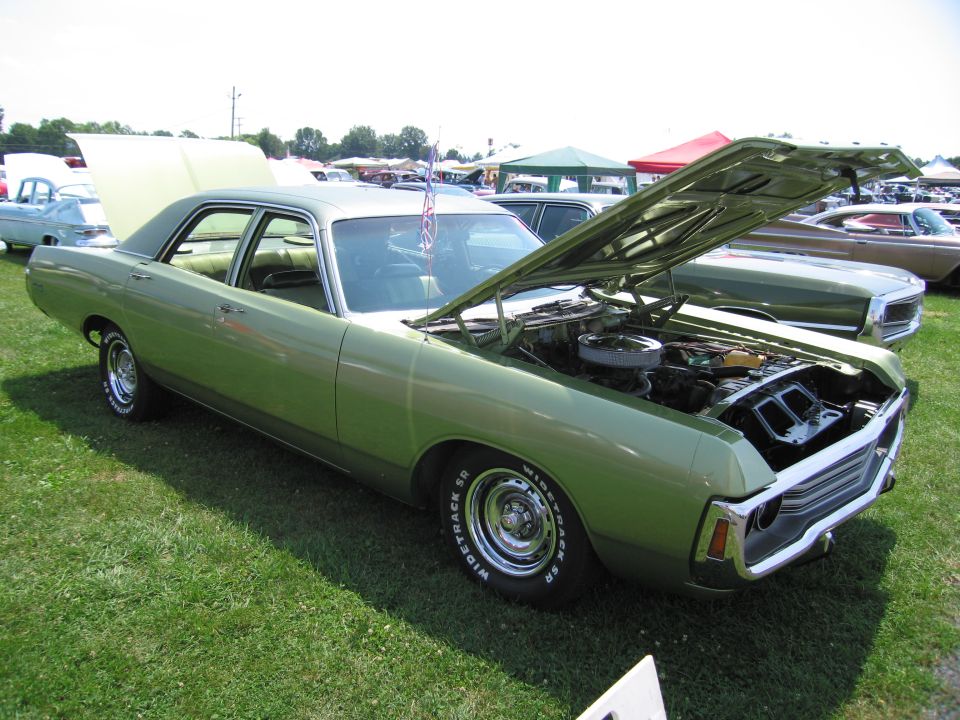 Green 1970s sedan with hood open, showing engine bay. Chrome grille and wheels visible