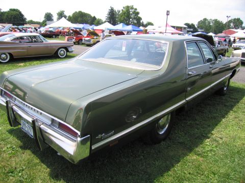 2001 Ford Crown Victoria - A green sedan with a prominent chrome bumper is parked on grass at an outdoor event. Other cars and tents are visible in the background.