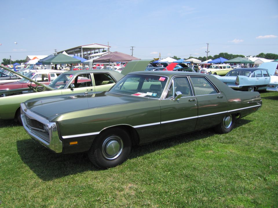 Green sedan parked on grass with other cars and tents in background