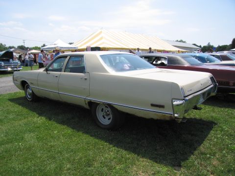 2001 Ford Crown Victoria - A tan sedan with significant rust on the lower body panels is parked on grass.