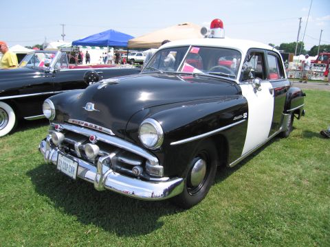 2001 Ford Crown Victoria - A vintage black and white police car is parked on grass with other vehicles and tents in the background.