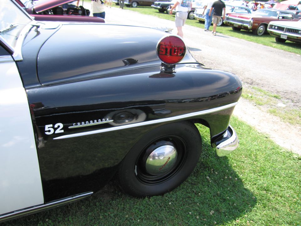 Black and white police car fender with '52 CRANBROOK' text and a red stop light on top