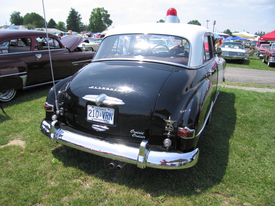 Black Plymouth with white roof and red light on top, parked on grass. Ontario license plate 210-VRN. Another car is parked to the left