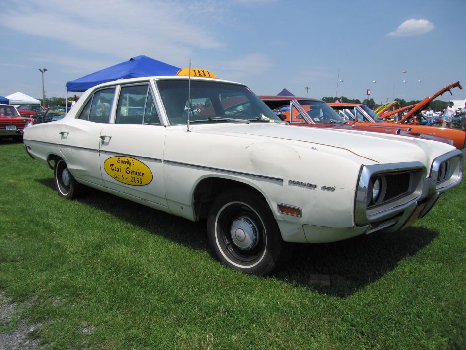 White taxi sedan with yellow oval Speedy's Taxi Service door decal and a yellow taxi sign on the roof