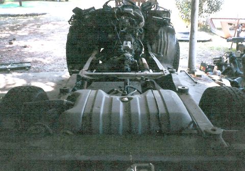 1983 Ford Bronco - The underside of a vehicle shows its engine, transmission, and fuel tank, with the rear tires visible.