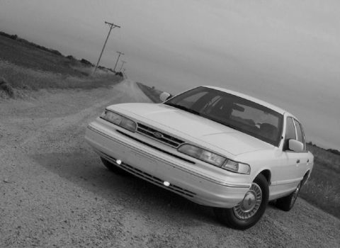 1996 Ford Crown Victoria - A white 1996 Ford Crown Victoria is parked on a dusty, rural road under an overcast sky.