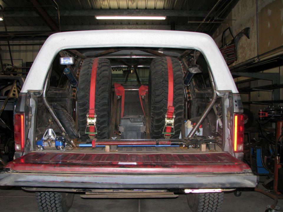 1980 Ford Bronco rear interior showing two spare tires secured with red straps, roll cage, and storage