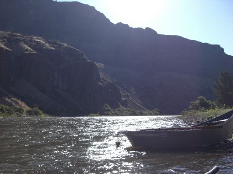 1993 Ford Bronco - A boat rests on the shore of a river, with a large, rocky cliff face dominating the background.