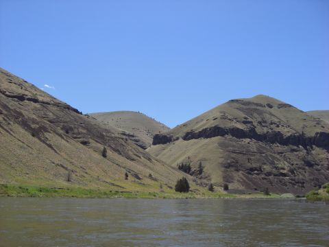 1993 Ford Bronco - A wide river winds through a valley flanked by dry, grassy hills under a bright blue sky.