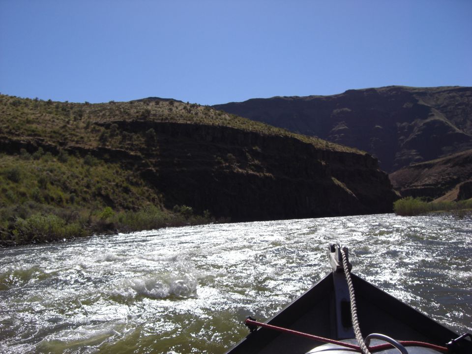 Boat bow on a sunlit river with mountains in background
