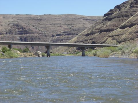 1993 Ford Bronco - A bridge spans a wide river, with , layered mountains rising behind it under a clear blue sky.