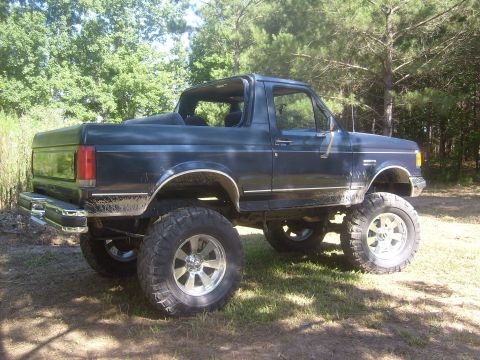 1989 Ford Bronco - A lifted 1989 Ford Bronco sits on a grassy area with trees in the background.
