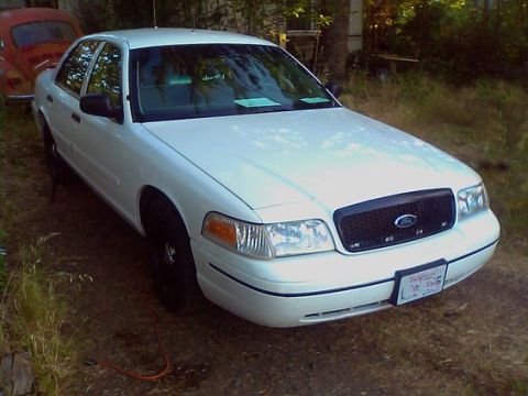 2000 Ford Crown Victoria - A white 2000 Ford Crown Victoria is parked in a grassy area next to a red Volkswagen Beetle.