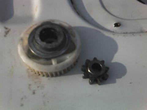 1996 Ford Bronco - Close-up of two gears, one large plastic and one small metal, on a white surface.