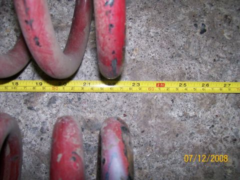 1984 Ford Bronco - A tape measure shows the length of red coil springs resting on a concrete surface.