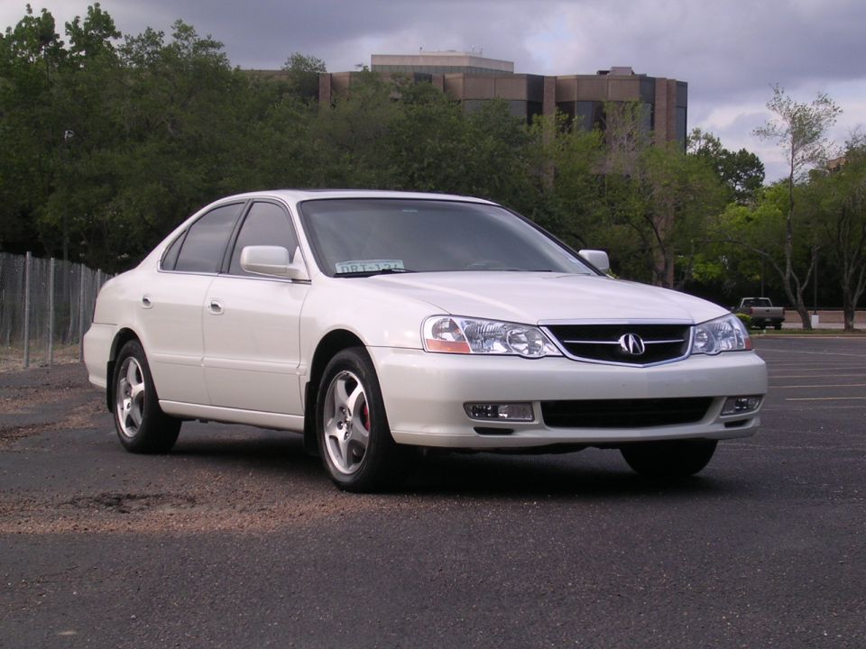 White Acura TL sedan low 3/4 front view in gravel lot with office building behind
