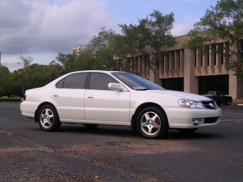 White Acura TL sedan side profile in parking lot by tan brick office building