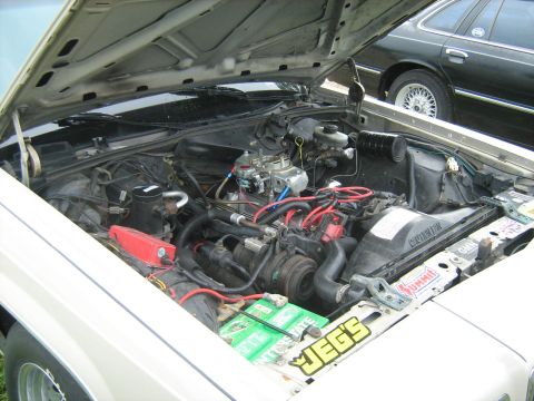 1988 Mercury Grand Marquis - The engine bay of a 1988 Mercury Grand Marquis, aftermarket parts and a glimpse of another vehicle in the background.