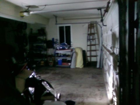 1995 Ford Bronco - A dimly lit garage scene contains storage shelves, a ladder, and a motorcycle partially visible in the foreground.