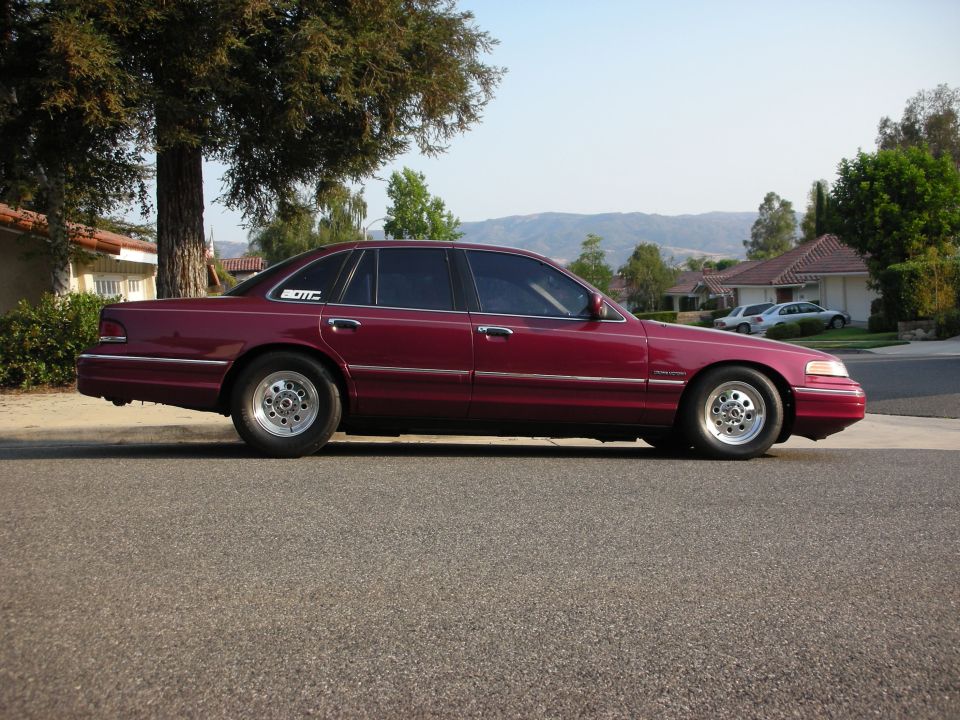 Side profile of a maroon Ford Crown Victoria on drag wheels on a suburban street