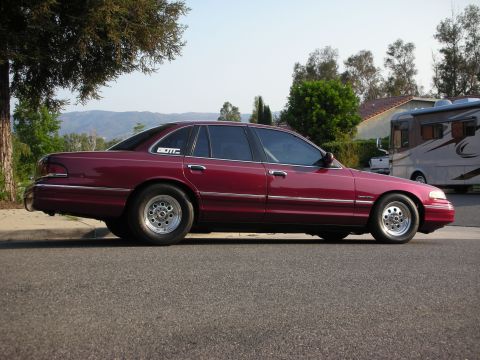1992 Ford Crown Victoria - A maroon sedan is parked on the side of a street with houses and trees in the background.