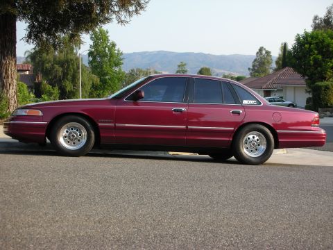 1992 Ford Crown Victoria - Side view of a red 1992 Ford Crown Victoria sedan aftermarket wheels and a subtle decal on the rear quarter panel.