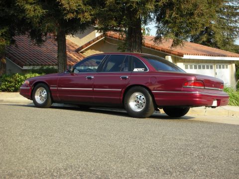 1992 Ford Crown Victoria - This maroon sedan is parked on a residential street, drag racing tires and a subtle sticker on the rear passenger door.