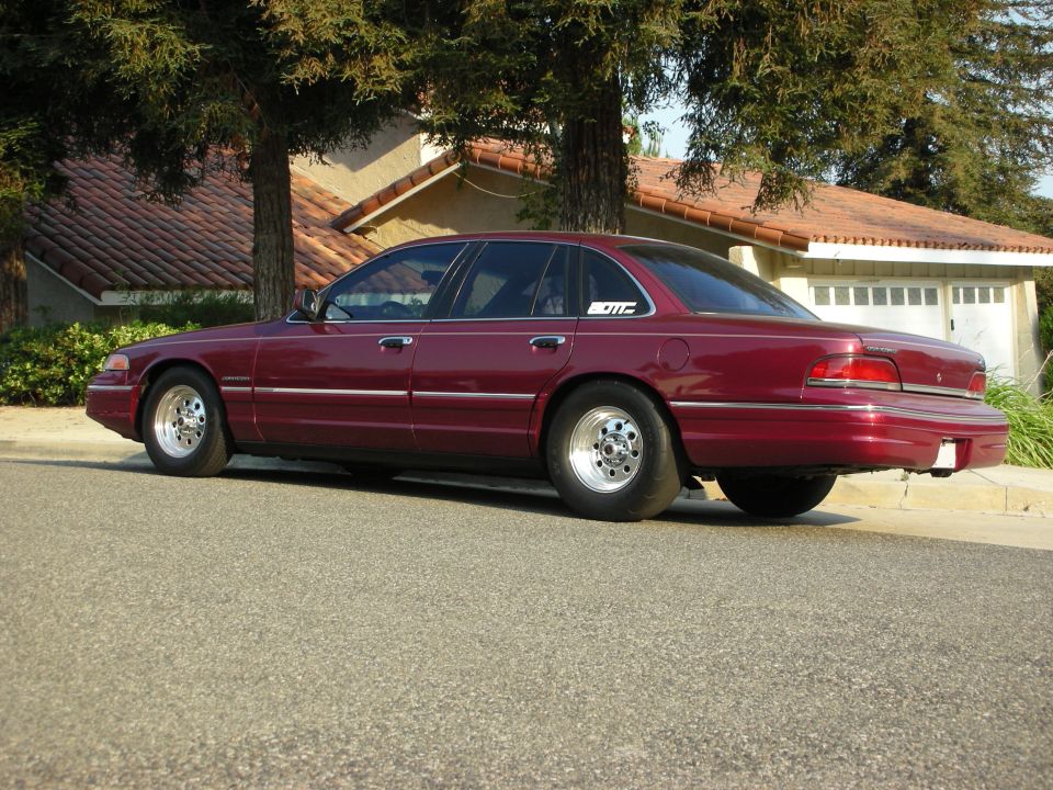 maroon sedan parked on street, has drag tires and a small sticker on the rear door