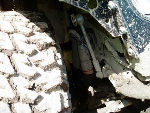 2000 Ford E350 - A close-up view of the heavily muddied front suspension and tire of a 2000 Ford E350. The image shows the tire tread, shock absorber, and p…