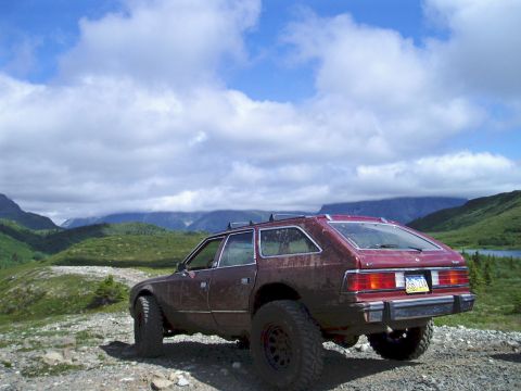 2000 Ford E350 - A maroon station wagon with off-road tires is parked on a gravelly hill overlooking a valley with mountains in the background.