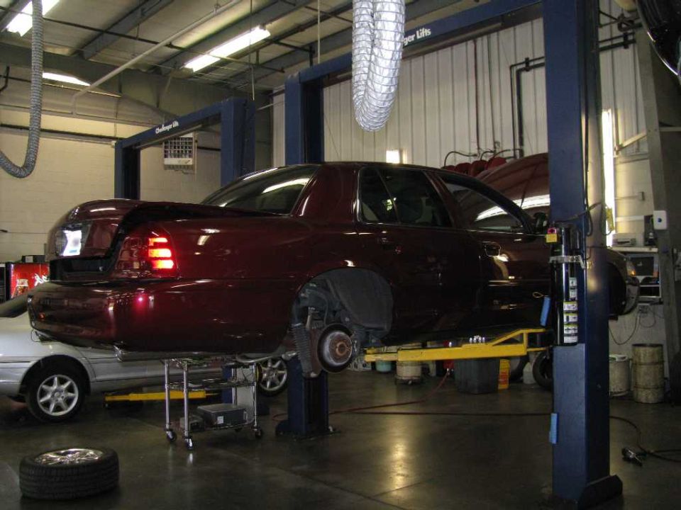 Dark red sedan on a car lift in a garage, rear view.