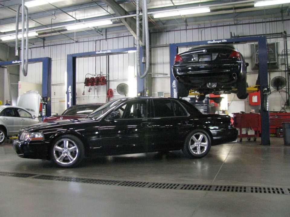 Black Mercury sedan in a garage with another Mercury sedan on a lift.