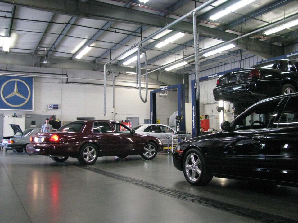 Dark red Mercury sedan and black sedan in a garage with a black sedan on a lift.