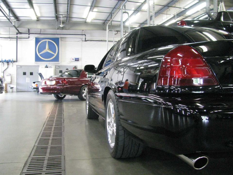 Rear view of a black sedan in a garage, with a red sedan in the background.
