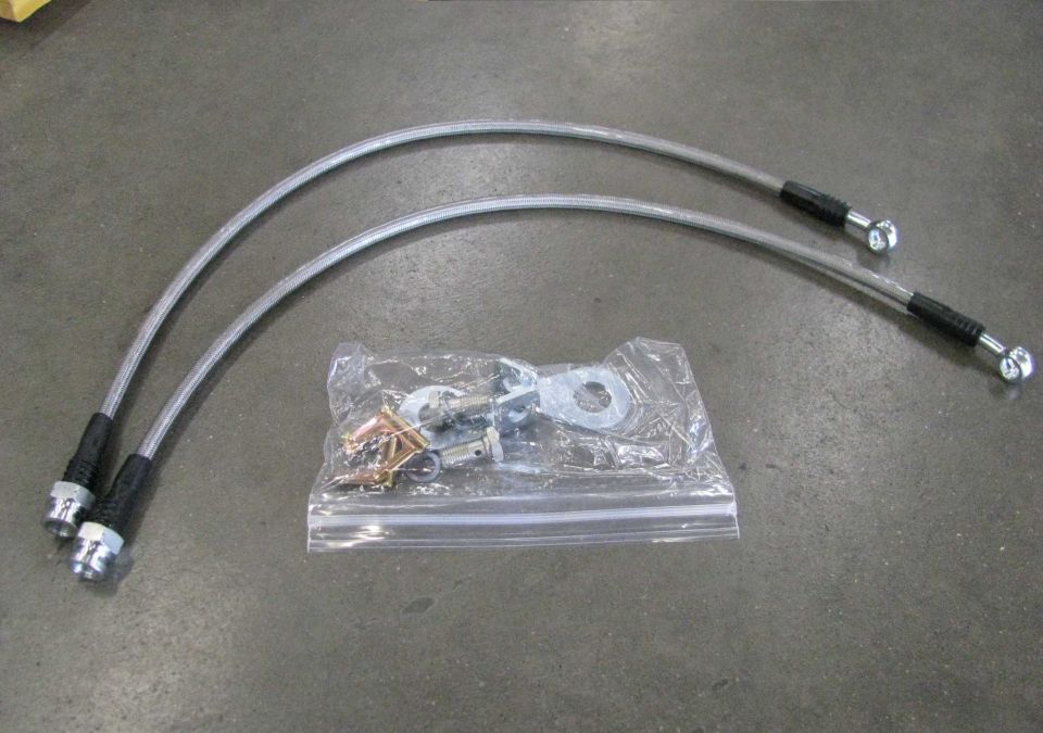 Two braided stainless steel brake lines and a bag of hardware on concrete