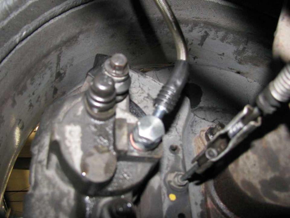 Close-up of a vehicle's brake caliper with brake lines and hardware.