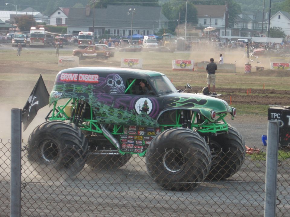Grave Digger monster truck with skull and flames graphic on a dirt track.