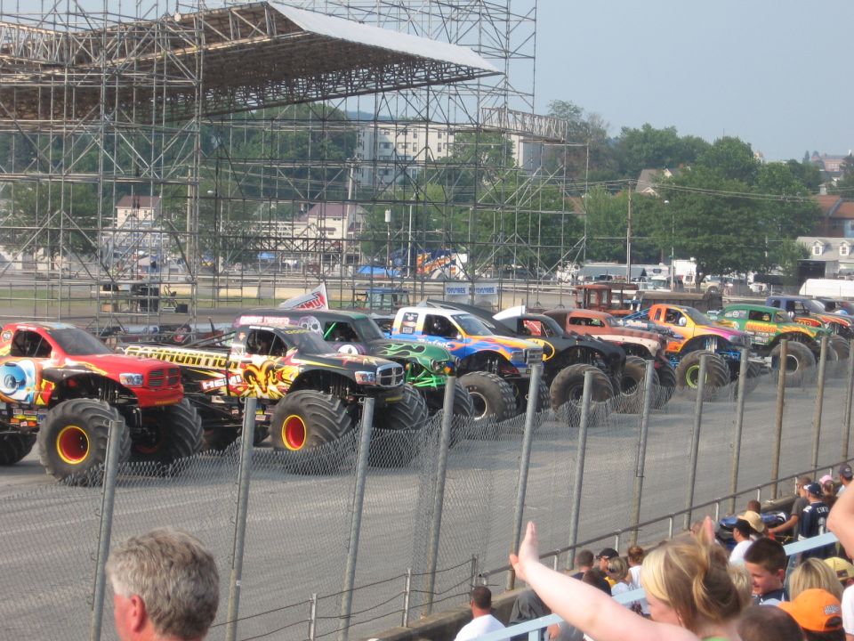 Monster trucks lined up in front of scaffolding.