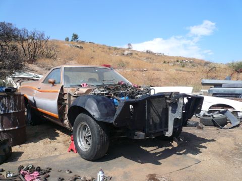1975 Ford Ranchero - A disassembled 1975 Ford Ranchero is parked outdoors in a dry, hilly area. The front end is missing its hood and grille, revealing the engi…