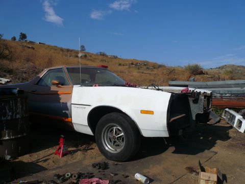 1975 Ford Ranchero - A partially restored 1975 Ford Ranchero is shown in a junkyard setting. The front end of the vehicle is disassembled, with the hood and gri…