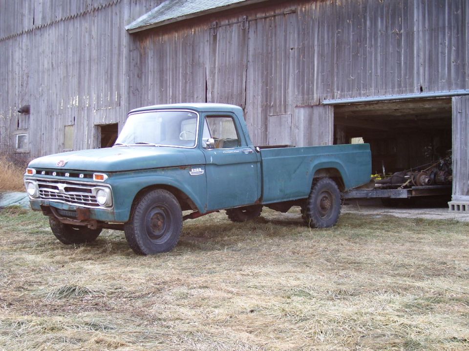 1966 Ford F-350 pickup truck, teal color, parked in front of a wooden barn.