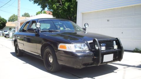 2000 Ford Crown Victoria - A black and white police car, identified as a 2000 Ford Crown Victoria, is seen from the front with a push bumper and light bar.