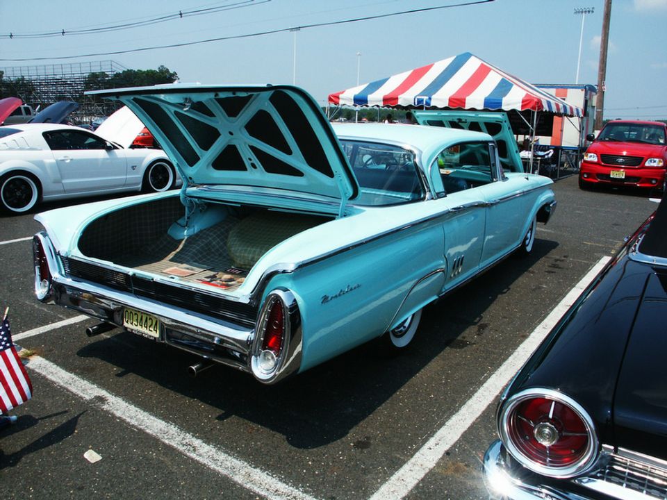Light blue 1959 Mercury Montclair with open trunk, parked next to a white Ford Mustang and a red Ford F-150