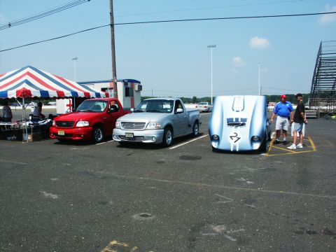 2001 Mercury Grand Marquis - Three vehicles are parked at an outdoor car show under a tent and bright sky.