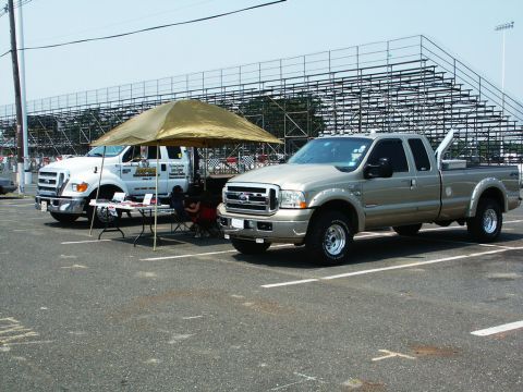 2001 Mercury Grand Marquis - Photo of two Ford Super Duty pickups parked by a vendor tent and bleachers at an outdoor event.