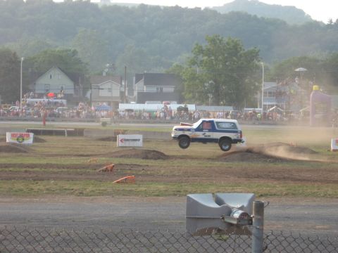 1984 Ford Bronco - Ford Bronco jumps a dirt mound at an event, kicking up dust.