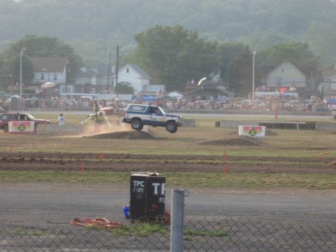 1984 Ford Bronco - A Ford Bronco is captured mid-air during an event, with spectators watching from the sidelines.