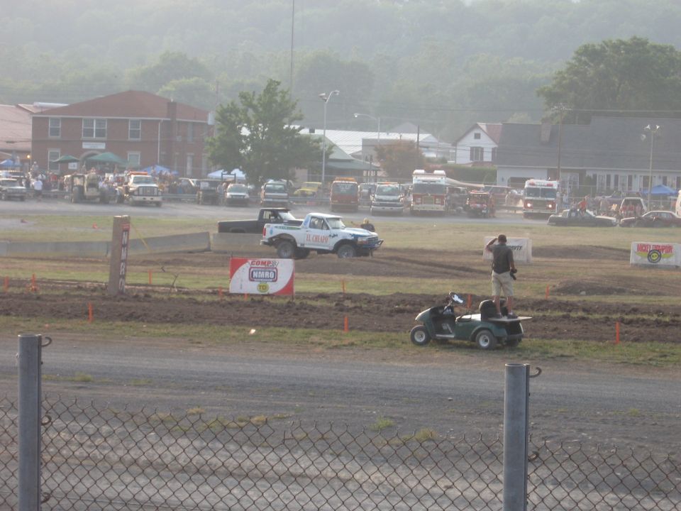 White pickup truck with green trim, mud-splattered, driving on a dirt track