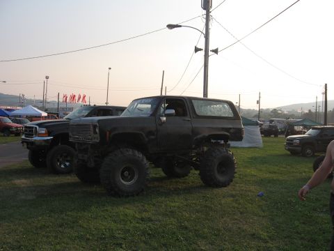 1984 Ford Bronco - A heavily modified SUV with oversized tires is parked on a grassy field.